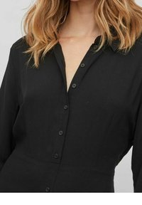 Černá košilová šaty s dlouhými rukávy, se límcem a hladkým, lehkým materiálem. Knoflíky jsou viditelné po celé délce přední části.