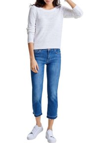 Pull en maille blanche avec un col rond, associé à un jean en denim bleu cropped et des baskets blanches. Style décontracté, design en maille texturée.