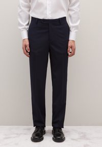 Pantalones de vestir azul marino hechos de tela lisa, con corte recto, trabillas para cinturón y cierre de un solo botón, combinados con zapatos negros.