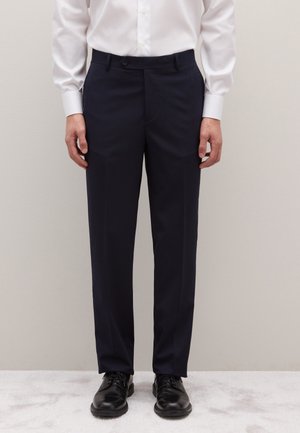 Pantalon de costume bleu marine en tissu lisse, doté d'une coupe droite, de passants pour ceinture et d'une fermeture par un seul bouton, assorti à des chaussures noires.