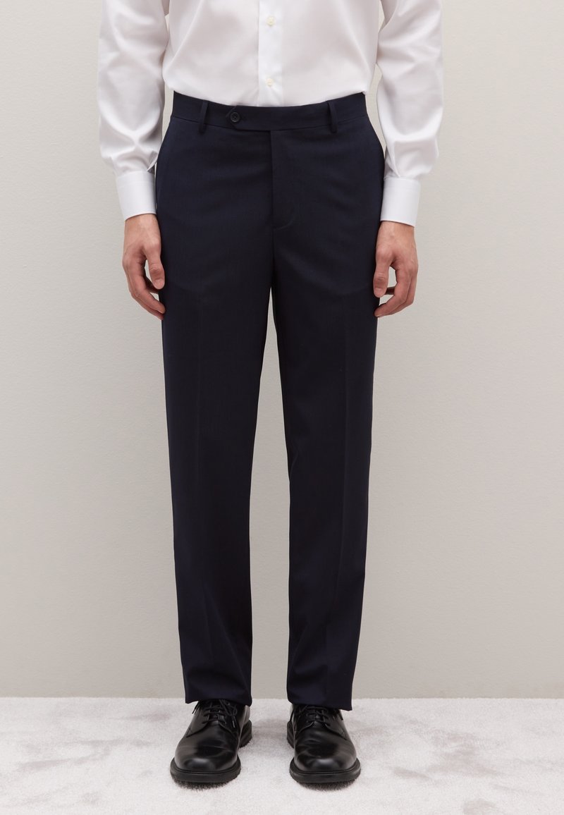 Pantalones de vestir azul marino hechos de tela lisa, con corte recto, trabillas para cinturón y cierre de un solo botón, combinados con zapatos negros.