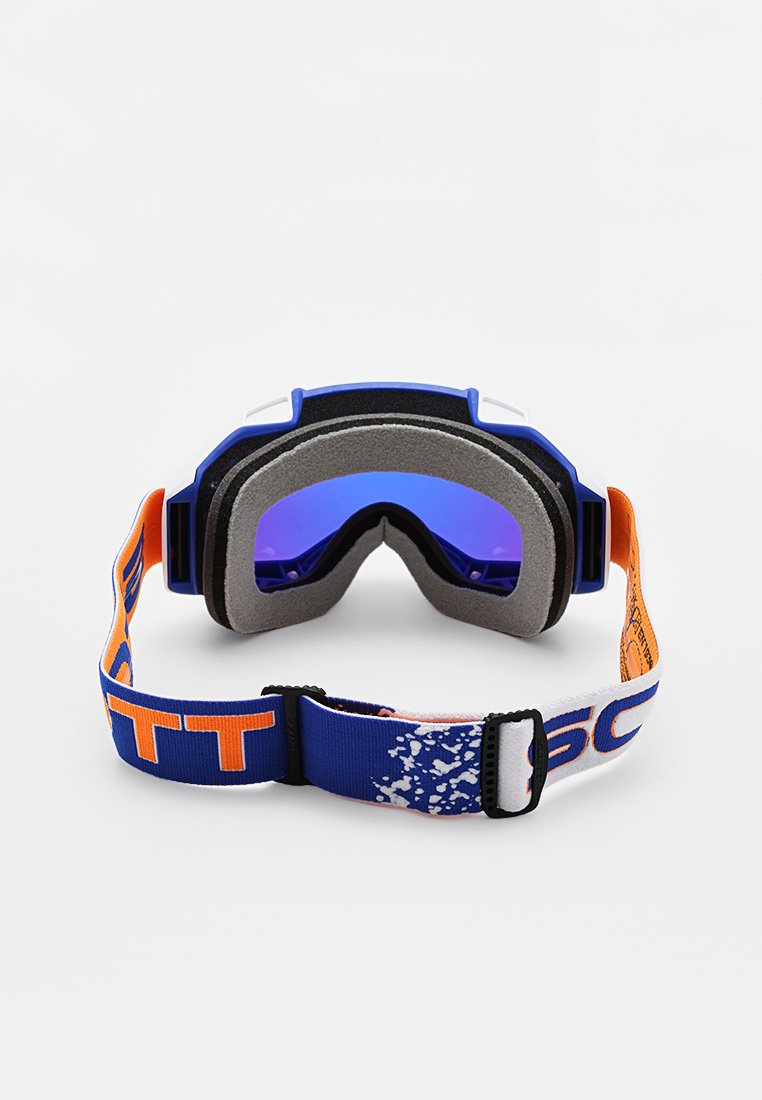 Gafas de esquí con marco azul, almohadillado de espuma gris y lente violeta. Cuenta con una correa azul y blanca con texto naranja y un patrón salpicado.
