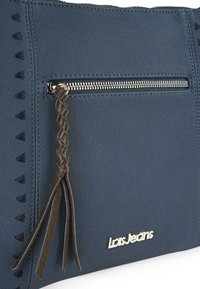 Bolso de tote texturizado en azul marino con un bolsillo frontal con cremallera, tirador de cremallera de cuero trenzado y logotipo dorado en la parte inferior. Presenta acentos triangulares.