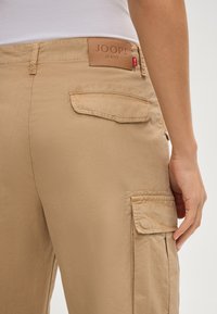 Kaki cargobroek met een soepele textuur, voorzien van opgestikte zakken, een leren label met "JOOP! JEANS" en een slanke pasvorm.