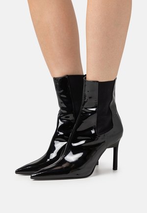 Czarne lakierowane botki na kostkę z zaostrzonymi noskami, błyszczącym wykończeniem i elastycznymi panelami po bokach. Posiadają szpilkowy obcas dla dodatkowego wzrostu.