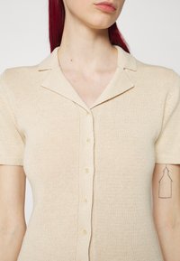 Top corto a maniche corte, color beige, in maglia con un finitura texturizzata e cinque bottoni sulla parte anteriore.