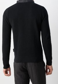 Black sweater with a textured knit pattern, long sleeves, and a ribbed hem. Features a contrasting smooth collar and a fitted design.