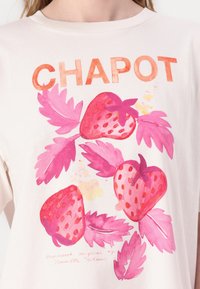 Licht beige t-shirt met een levendige roze aardbeienprint en de tekst "CHAPOT" erboven. Zacht katoenen stof met een klassieke ronde hals.