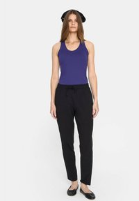 Fioletowy top na ramiączkach, czarne spodnie materiałowe z sznurkiem, płaskie czarne buty. Gładki materiał, slim fit, prosty design, minimalne akcenty i brak wyraźnych wzorów.