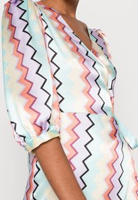 Mångfärgad klänning med ett zigzag-mönster i pastellnyanser av blått, rosa och lavendel. Texturerat tyg med V-ringning och puffärmar.