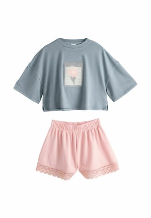Camiseta corta azul con parche de flor rosa combinada con pantalones cortos rosas con cintura elástica y encaje en el dobladillo.