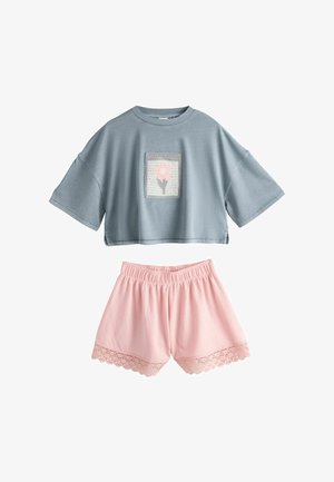Camiseta corta azul con parche de flor rosa combinada con pantalones cortos rosas con cintura elástica y encaje en el dobladillo.
