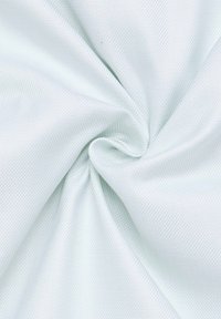 Tessuto verde chiaro testurizzato con un motivo intrecciato, che mostra un drappeggio morbido e flessibile, piegato per evidenziare profondità e dimensione.