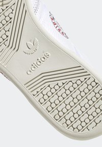 Suola di una sneaker bianca con presa testurizzata, caratterizzata da un logo adidas prominente e dettagli a motivo lungo il bordo. Design pulito e sportivo.