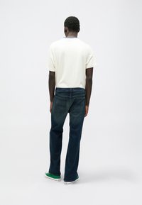 Λευκό T-shirt κοντό μανίκι συνδυασμένο με σκούρο μπλε τζιν παντελόνι. Το τζιν έχει κλασική εφαρμογή και δύο πίσω τσέπες. Πράσινα αθλητικά παπούτσια ολοκληρώνουν την εμφάνιση.