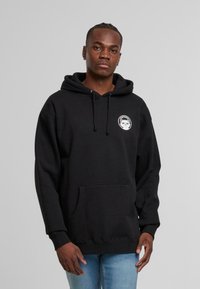 Felpa con cappuccio nera in cotone; presenta una tasca frontale e un logo rotondo con una grafica di panda sul petto.