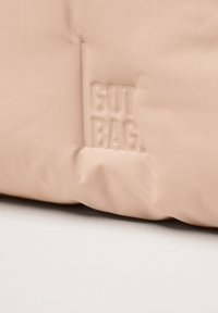 Torba z tkaniny w kolorze brzoskwiniowym o teksturowanej powierzchni, z wytłoczonym logo "GOT BAG." i prostym, minimalistycznym designem.