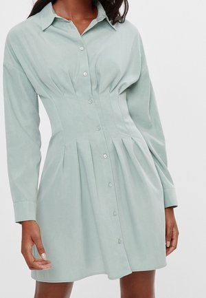 Vestito verde chiaro con bottoni, maniche lunghe, corpetto aderente, gonna plissettata e tessuto morbido. Presenta un design con collo classico.