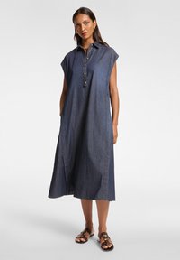 Abito camicetta in denim blu scuro, con maniche corte, chiusura con bottoni frontale e tasche laterali. Tessuto liscio con una vestibilità rilassata e fluida.