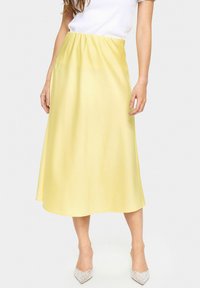 Yellow satin midi skirt with an elastic waistband, featuring a smooth texture and a flared silhouette, paired with rhinestone-accented heels.