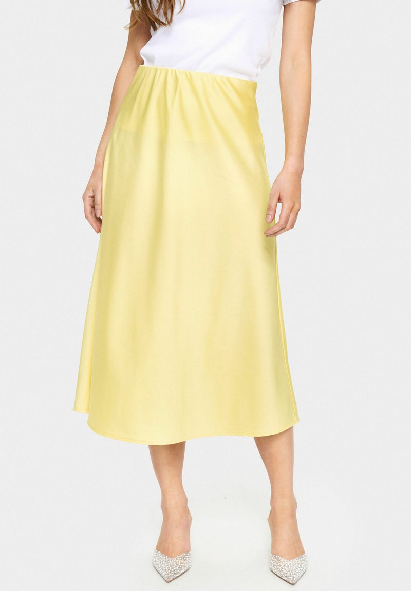 Yellow satin midi skirt with an elastic waistband, featuring a smooth texture and a flared silhouette, paired with rhinestone-accented heels.