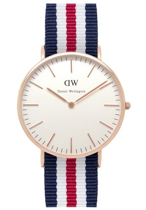 Rund Daniel Wellington ur med hvid urskive, rosaguldfarvet urkasse, minimalistiske timeindikatorer og navy, hvid og rød stribet stofrem.