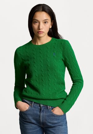 Green cable-knit sweater with a round neckline and ribbed cuffs. Features a small blue logo on the chest. Worn with blue denim jeans.
