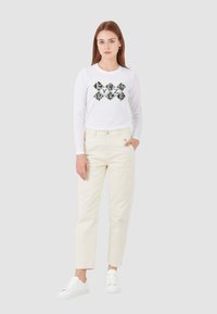 Camicia bianca a maniche lunghe con un motivo a rombi, abbinata a pantaloni color crema e sneakers bianche. Design semplice e casual.