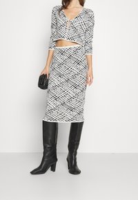 Tvådelad outfit bestående av en kort svart och vit mönstrad topp med v-ringning och en matchande lång pennkjol. Kombinerad med svarta knähöga stövlar.