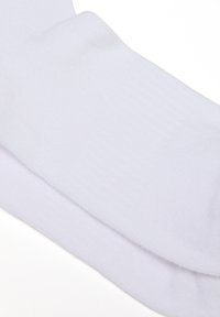 Un par de calcetines de algodón blanco liso doblados con puños acanalados sobre un fondo blanco.