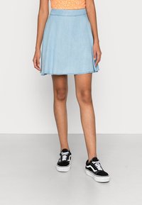 Hellblauer Denimrock mit ausgestelltem Design, ausgefranstem Saum und tailliertem Bund, kombiniert mit schwarzen und weißen Turnschuhen. Glatte Textur.