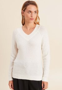 Weißer V-Ausschnitt-Pullover aus strukturiertem Strickstoff mit subtilen gesprenkelten Akzenten. Verfügt über lange Ärmel und einen gerippten Saum.