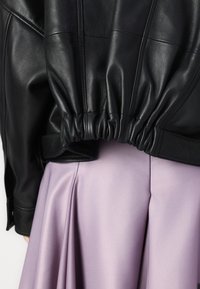 Casaco de pele preto com detalhes de bainha franzida, combinado com uma saia de cetim lavanda suave com pregas para movimento e textura.