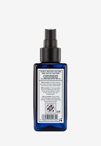 Blå glas sprayflaska med en svart pumpkork. Etiketten på baksidan innehåller text på flera språk och symboler för rena ingredienser.