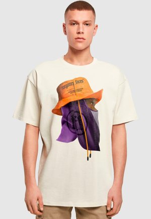 Cremefarvet t-shirt med et grafisk print af en person i en lila maske og en orange bøttehat med sort tekst. Korte ærmer og afslappet pasform.