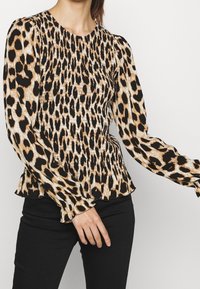 Blusa a maniche lunghe con stampa leopardata, scollo rotondo, texture arricciata e orlo con volant; presenta colori in contrasto nero e beige.