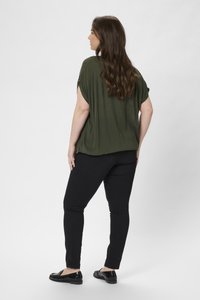Vihreä oliivinvärinen lyhythihainen paita, rento malli, yhdistetty mustiin skinny-farkkuihin ja kiiltäviin mustiin loafer-kengiin. Sujuva pinta, rento muotoilu.