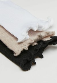 Tři páry ponožek po kotníky v bílé, béžové a černé barvě, s ribovanou strukturou a volánkovými okraji.