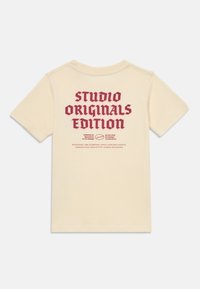 Krémový bavlněný tričko s krátkým rukávem, s výrazným červeným potiskem na zadní straně: "STUDIO ORIGINALS EDITION."