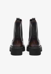 Botas de tobillo de cuero negro con una textura suave, suelas negras gruesas, tiradores en la parte posterior y un acabado ligeramente brillante en la parte superior.