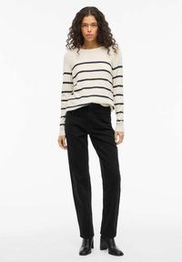 Sweter w paski w kolorze kremowym i granatowym, o luźnym kroju. Połączony z prostymi czarnymi dżinsami i czarnymi butami na obcasie. Gładka faktura i casualowy design.