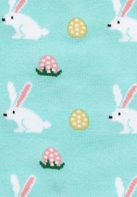 Lapins blancs aux oreilles roses et œufs de Pâques à pois jaune et rose sur un fond en tissu tricoté bleu clair.