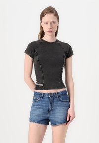 Crni uski crop top s kratkim rukavima i vidljivim šavovima, uparen s traper šortsevima svijetloplave boje.