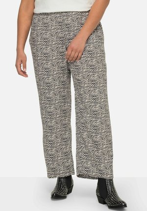 Wijdvallende pantalons in een beige en zwart zebrapatroon, met een gladde textuur en een elastische tailleband. Draagt met studs versierde enkellaarsjes.
