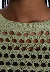 Top lavorato a maglia verde chiaro con un design ad intersezione aperta, caratterizzato da ritagli circolari e dettagli testurizzati attorno al collo.