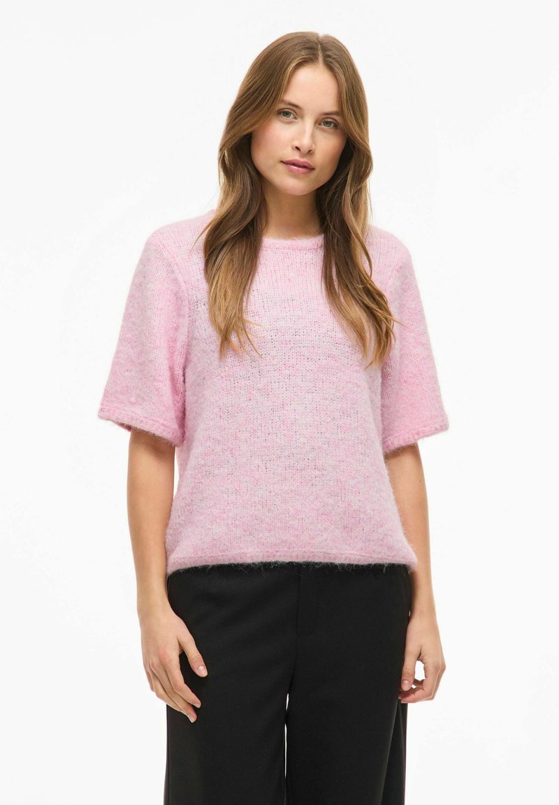 Rozā, īsroku džemperis no mīksta, pūkaina materiāla ar brīvu piegriezumu, apaļu izgriezumu un smalkām tekstūras variācijām.