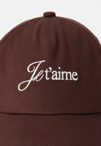 Brown cotton baseball cap featuring white embroidered text "Je t'aime" on the front. Design includes a stitched top button and visor.