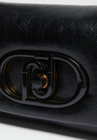Crni intrigantni faux kožni novčanik koji ima elegantnu, sjajnu crno-zlatnu kopču s logotipom. Površina ima teksturirani izgled s finim linijama.