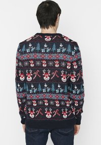 Mörkblå stickad tröja med festliga mönster av snögubbar, renar, godiskäppar och träd i rött, blått och vitt mot en mörk bakgrund.