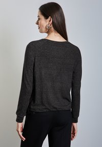Top negro de manga larga con un tejido texturizado que presenta sutiles destellos metálicos. Cuello redondeado y mangas raglán, combinado con pantalones oscuros.